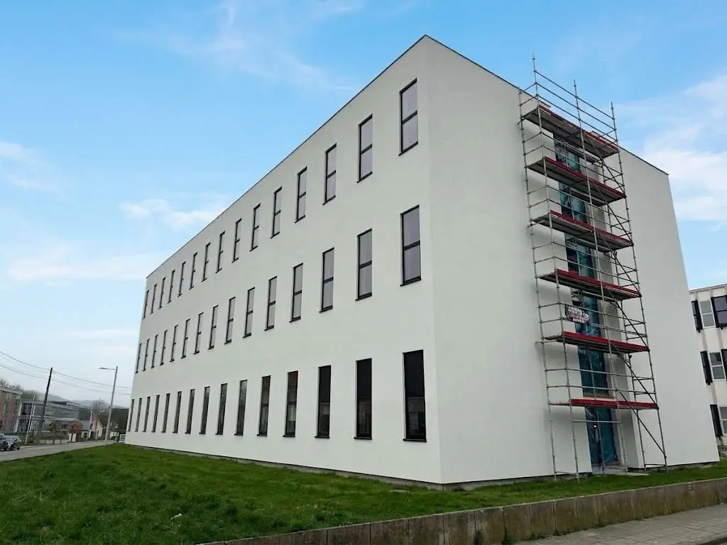 L’immeuble terminé, façade blanche, avec une dernière tour d’échafaudage, à Mons